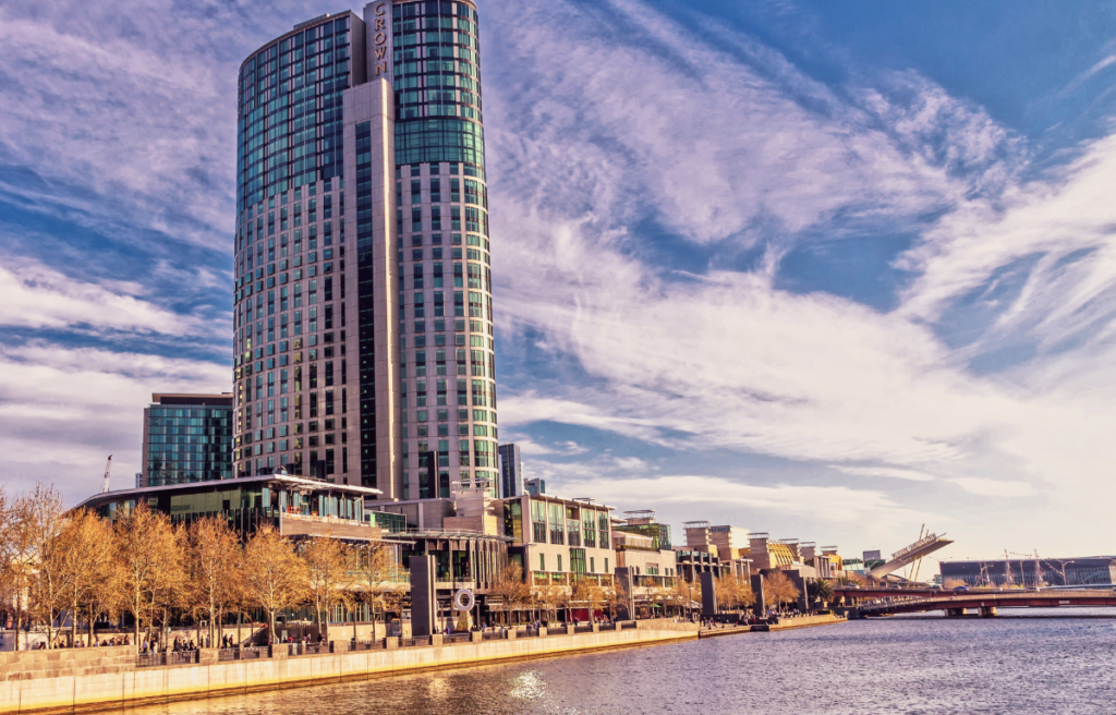 Crown Towers Melbourne, a high-rise luxury hotel situated along the Yarra River. The building features a modern architectural design with sleek glass windows and a curved structure. 